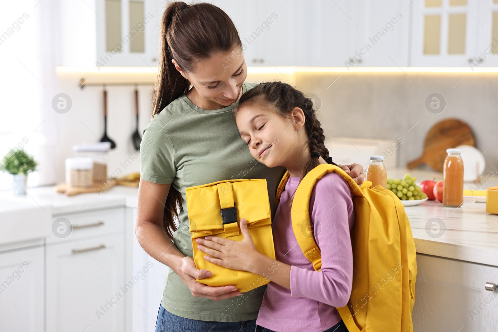 Photo of Smiling mother and her daughter with lunch bag in kitchen. Preparing for school