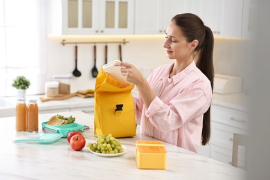 Photo of Woman with bag packing school lunch box and healthy food at white marble table in kitchen