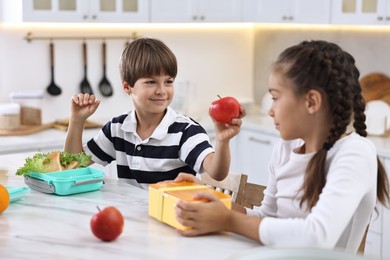 Cute children preparing school lunch boxes with healthy food at white marble table in kitchen