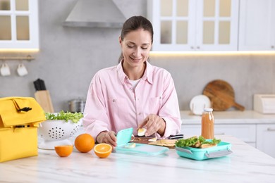 Smiling woman making snacks for school lunch box at white marble table in kitchen