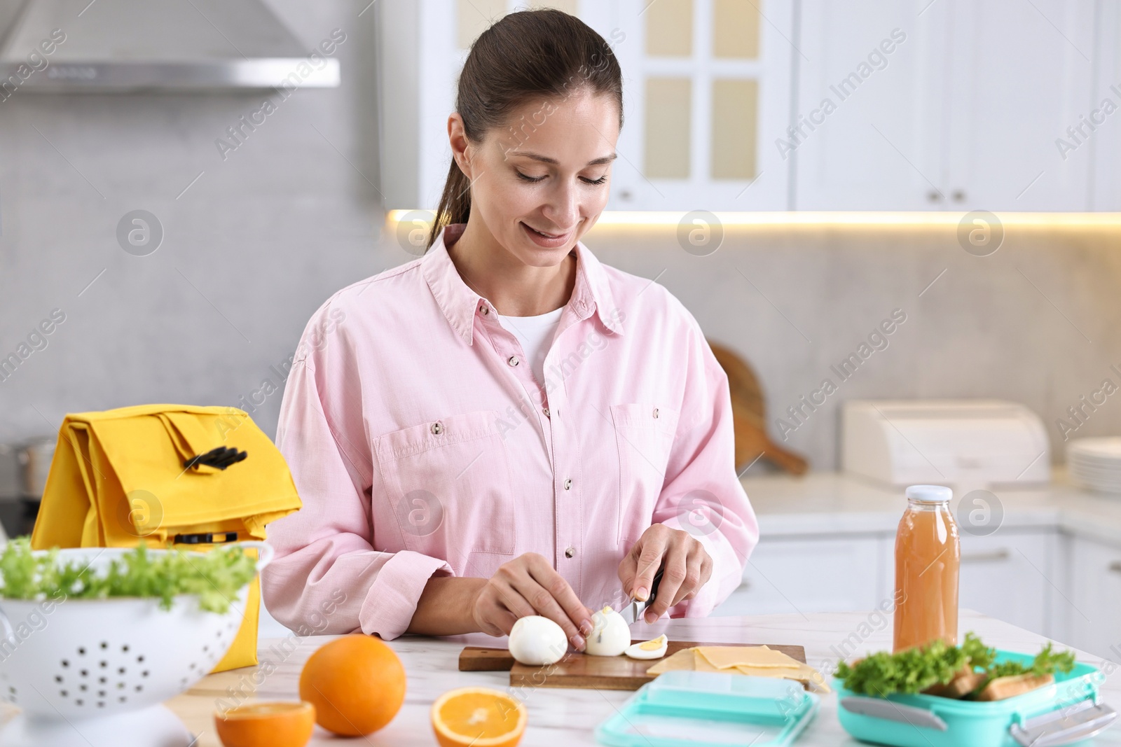 Photo of Smiling woman making snacks for school lunch box at white marble table in kitchen