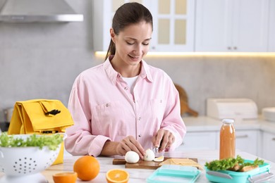 Smiling woman making snacks for school lunch box at white marble table in kitchen