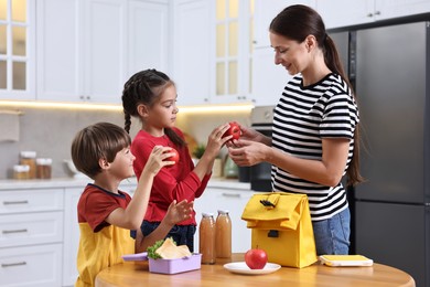 Photo of Mother and her cute children preparing school lunch box with healthy food at wooden table in kitchen