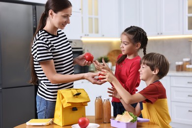 Mother and her cute children preparing school lunch box with healthy food at wooden table in kitchen