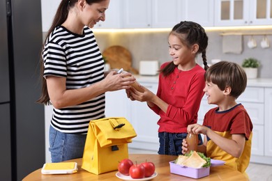 Mother and her cute children preparing school lunch box with healthy food at wooden table in kitchen