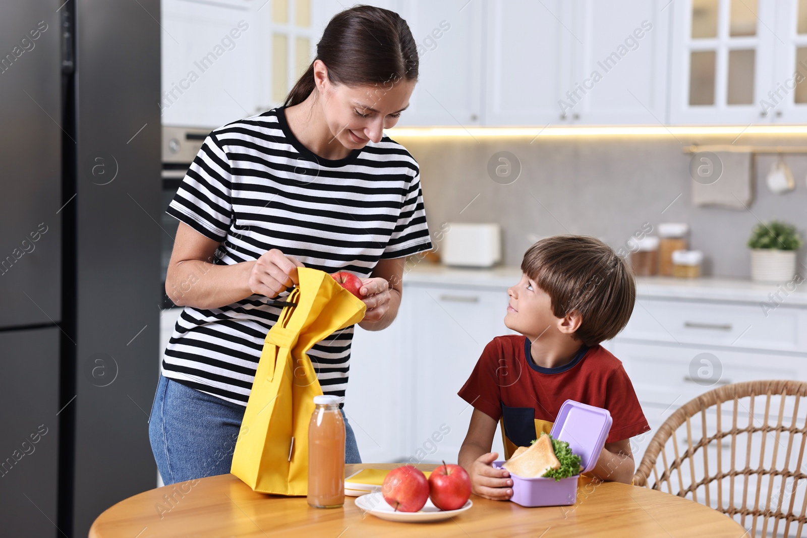 Photo of Mother and her cute son preparing lunch box with healthy food at wooden table in kitchen