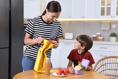 Mother and her cute son preparing lunch box with healthy food at wooden table in kitchen