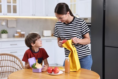 Photo of Mother and her cute son preparing lunch box with healthy food at wooden table in kitchen