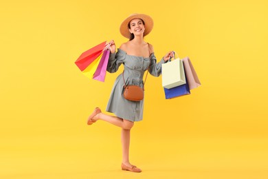 Smiling woman with colorful shopping bags on yellow background