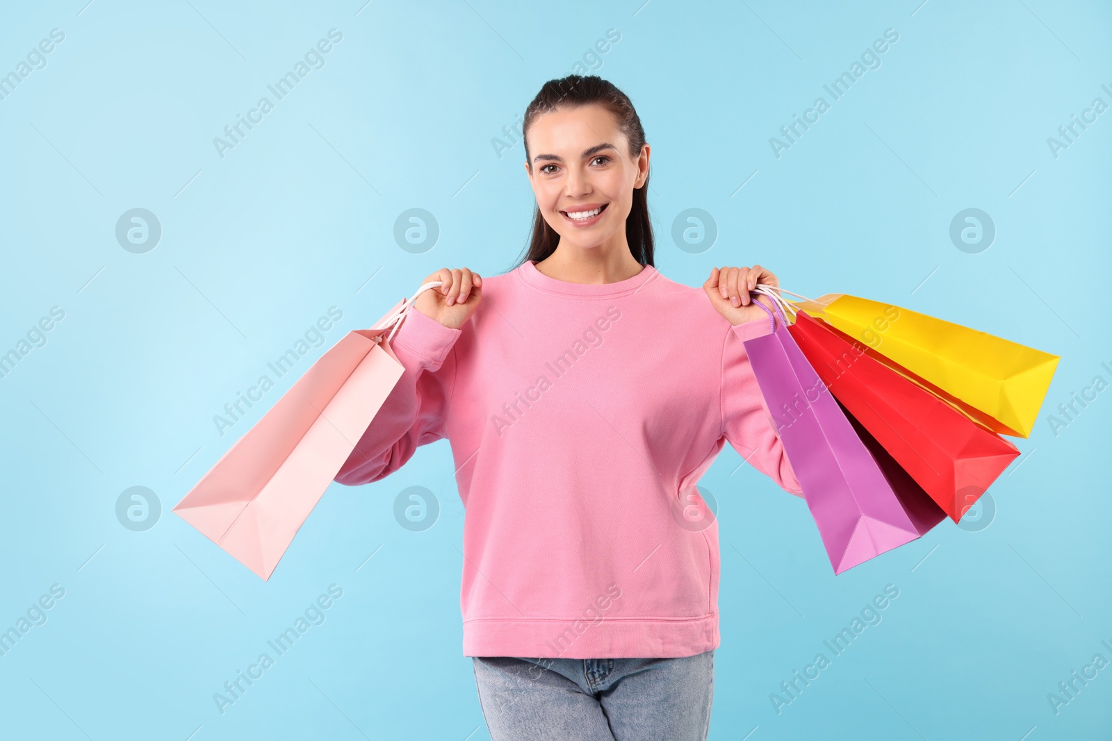 Photo of Smiling woman with colorful shopping bags on light blue background