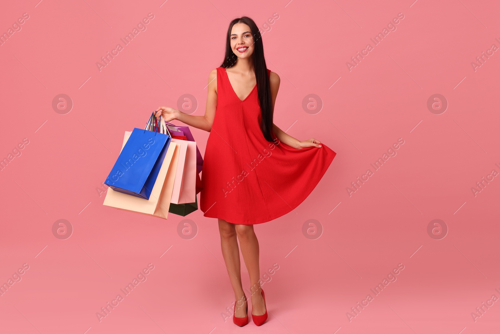 Photo of Smiling woman with colorful shopping bags on pink background