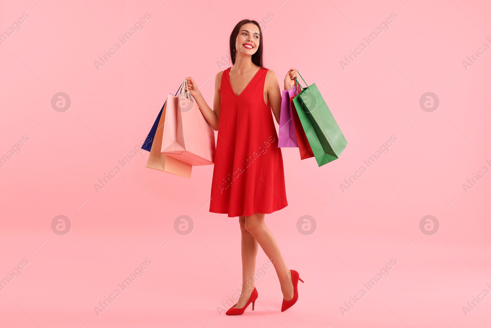 Photo of Smiling woman with colorful shopping bags on pink background