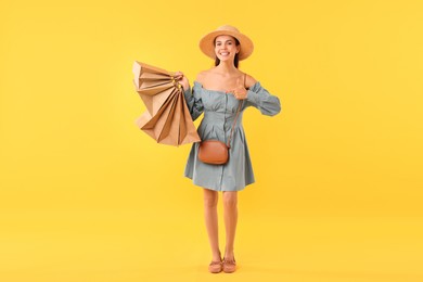 Smiling woman pointing at shopping bags on yellow background