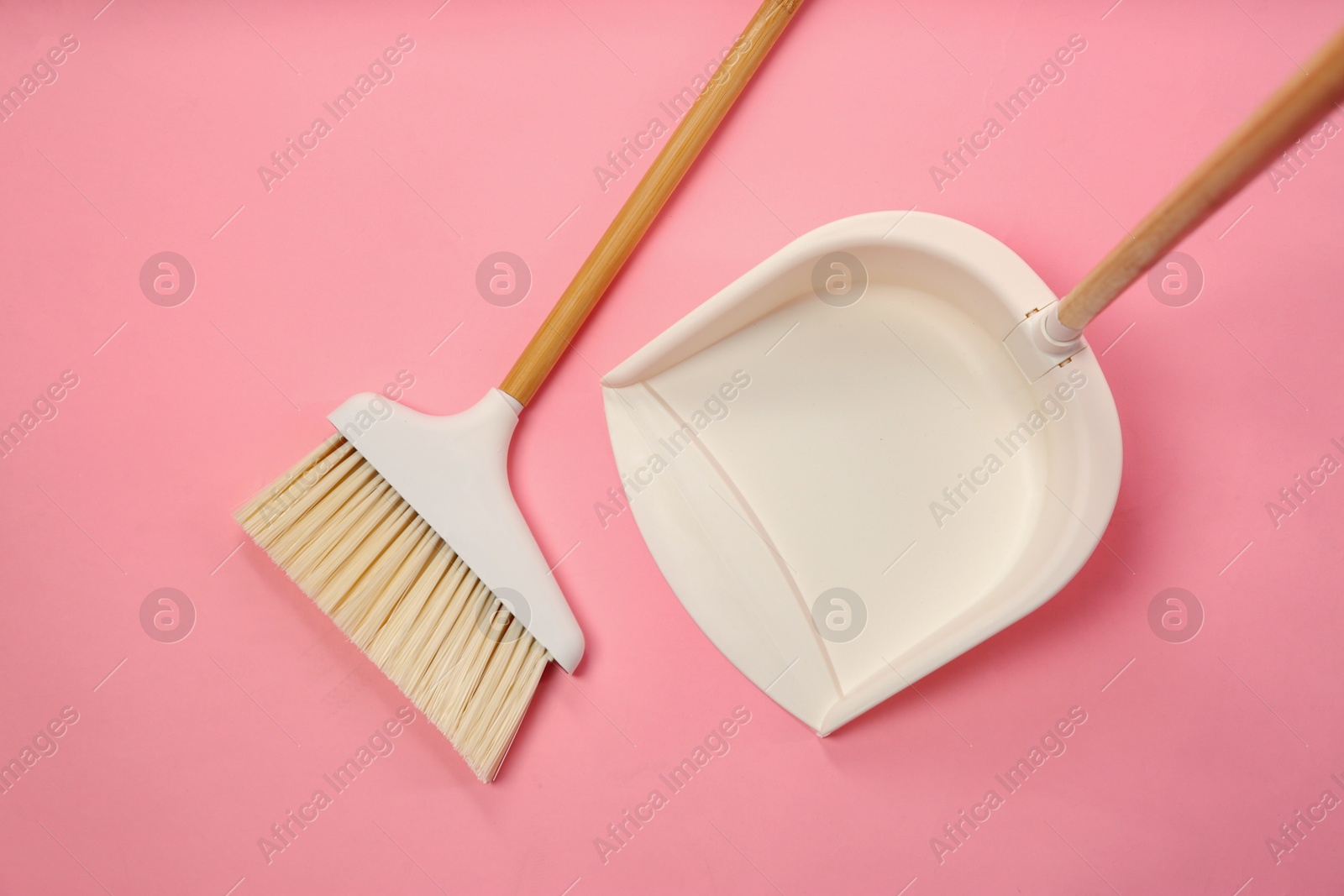 Photo of Cleaning broom and dustpan on pink background, flat lay