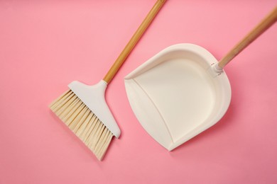 Photo of Cleaning broom and dustpan on pink background, flat lay