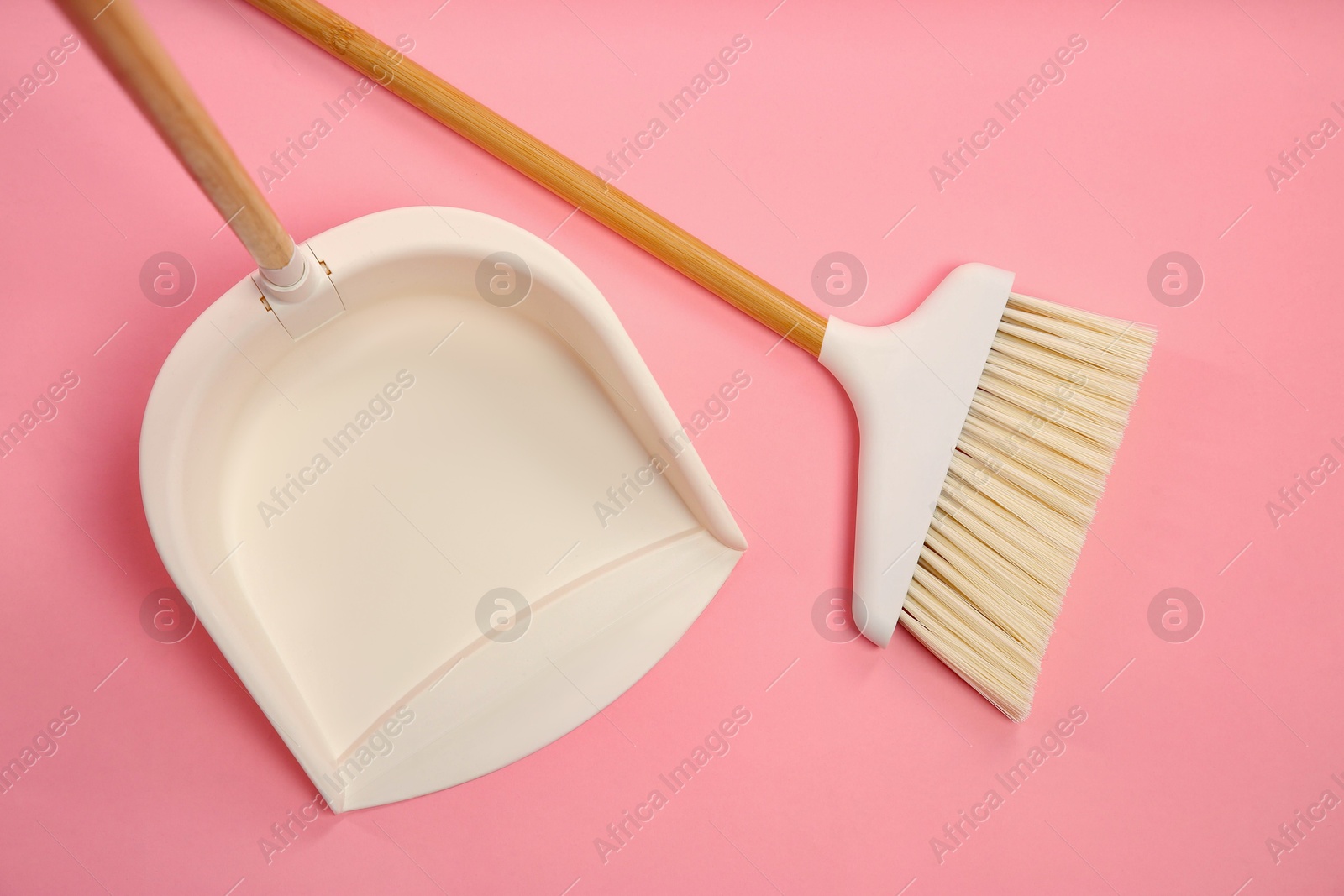 Photo of Cleaning broom and dustpan on pink background, flat lay