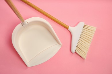 Photo of Cleaning broom and dustpan on pink background, flat lay