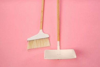 Photo of Cleaning broom and dustpan on pink background, flat lay