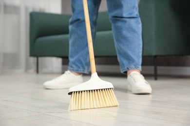 Photo of Woman with broom sweeping floor indoors, closeup