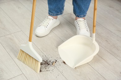 Photo of Woman with broom and dustpan cleaning floor indoors, closeup