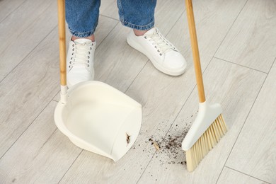 Photo of Woman with broom and dustpan cleaning floor indoors, closeup