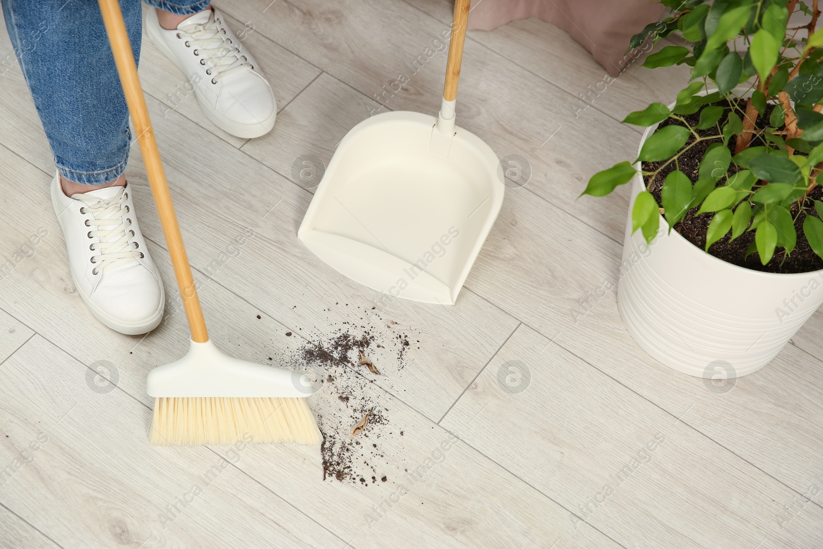 Photo of Woman with broom and dustpan cleaning floor indoors, closeup