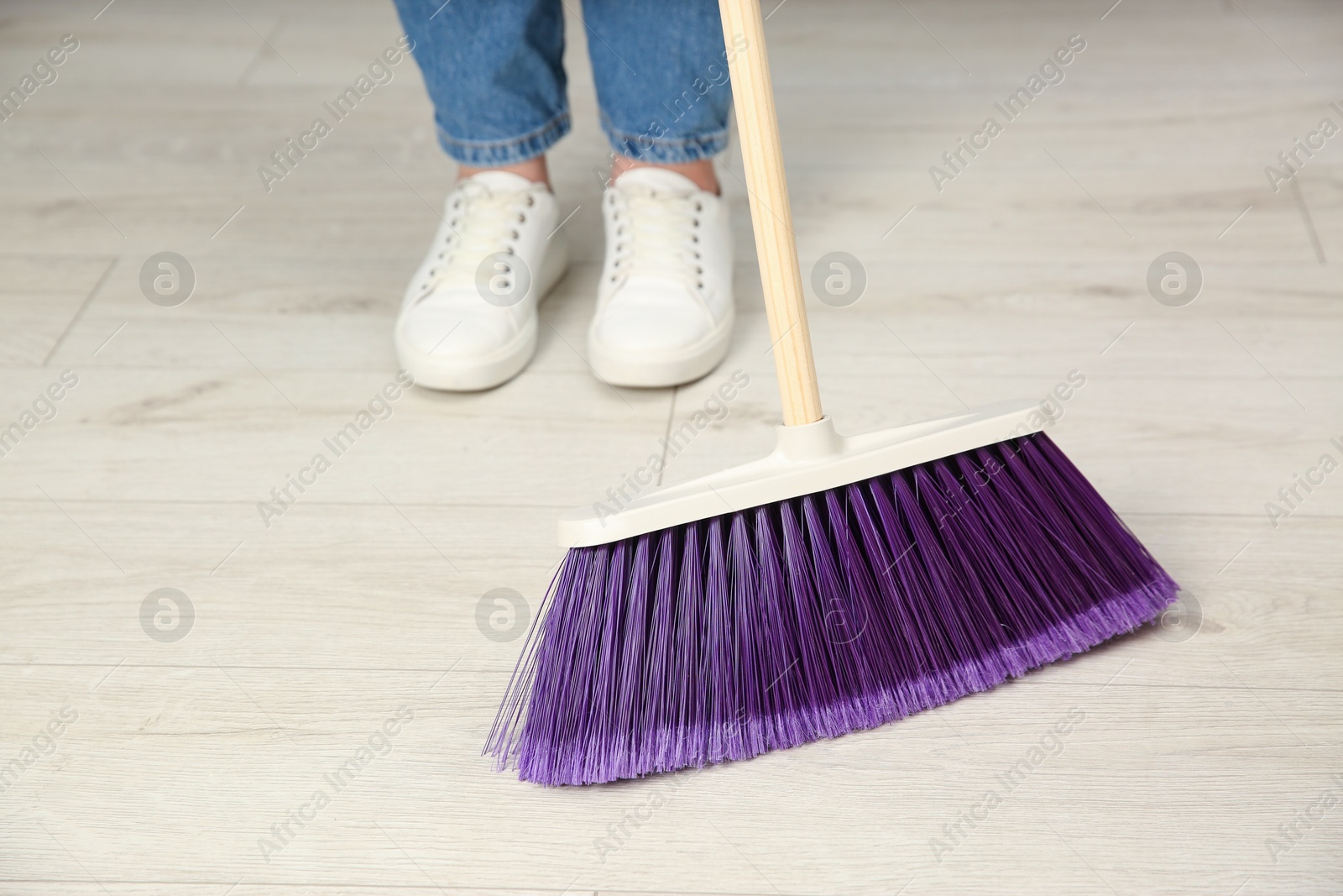 Photo of Woman with broom sweeping floor indoors, closeup