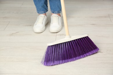 Photo of Woman with broom sweeping floor indoors, closeup