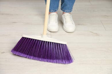 Photo of Woman with broom sweeping floor indoors, closeup