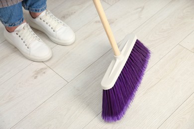 Photo of Woman with broom sweeping floor indoors, closeup