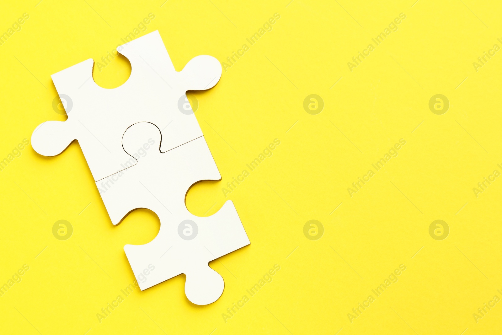 Photo of White puzzle pieces on yellow background, top view. Space for text