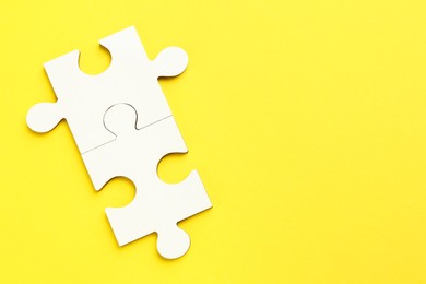 Photo of White puzzle pieces on yellow background, top view. Space for text