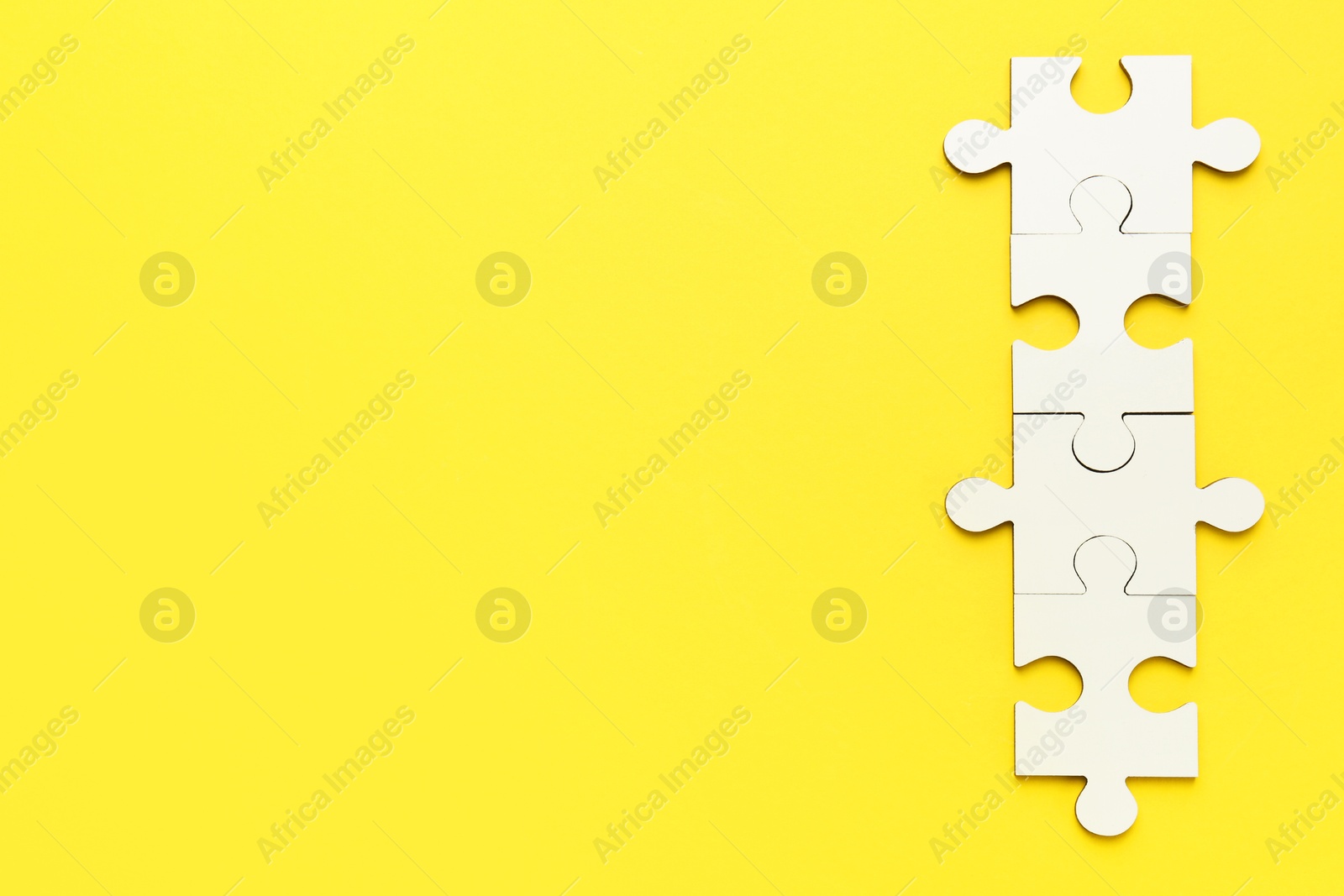 Photo of White puzzle pieces on yellow background, top view. Space for text