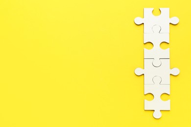 Photo of White puzzle pieces on yellow background, top view. Space for text