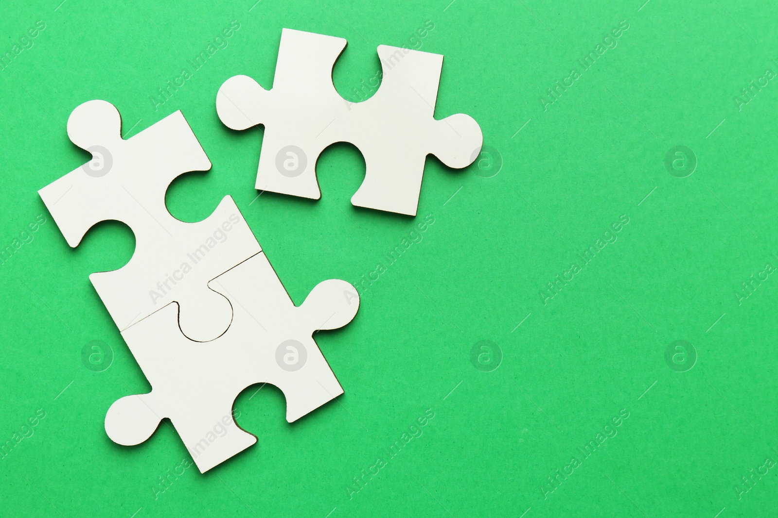 Photo of White puzzle pieces on green background, top view. Space for text