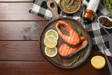 Tasty grilled salmon steaks, lemon and spices on wooden table, flat lay. Space for text