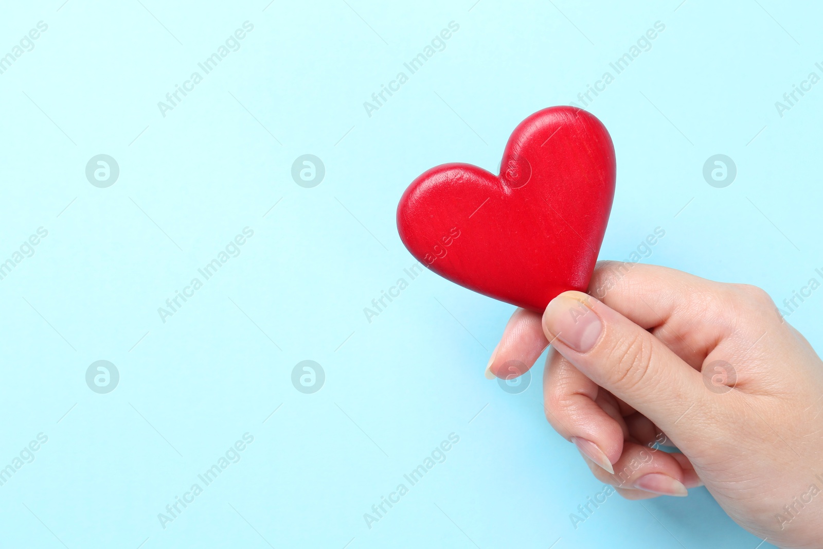 Photo of Woman with red heart on light blue background, closeup. Space for text