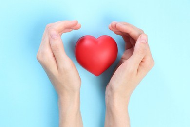 Photo of Woman holding red heart on light blue background, top view