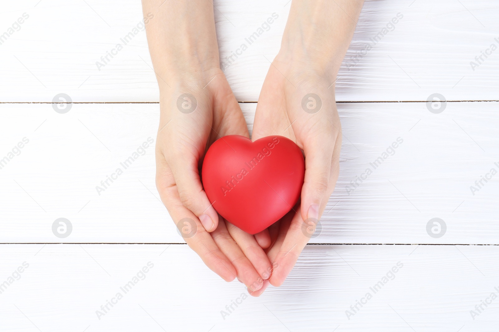 Photo of Woman holding red heart on white wooden background, top view