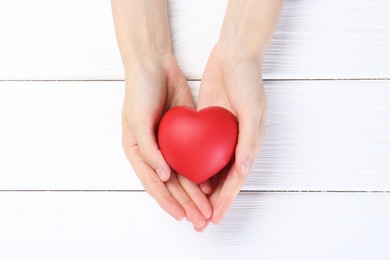 Photo of Woman holding red heart on white wooden background, top view