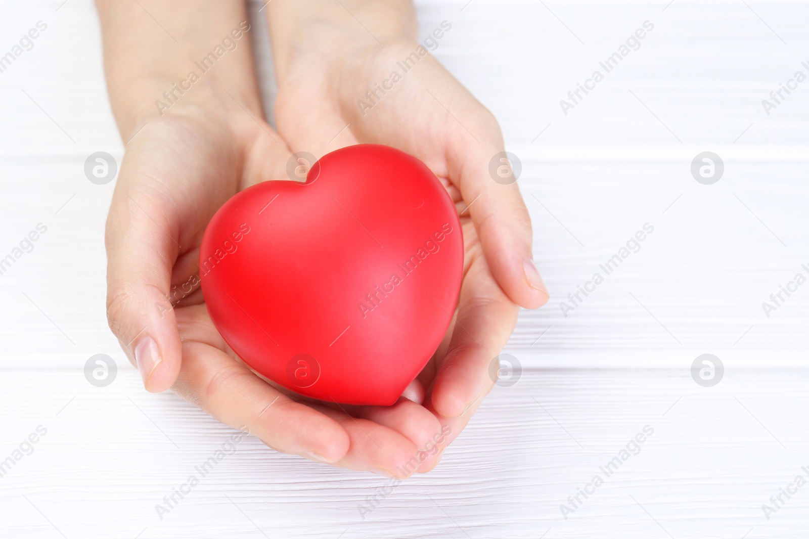 Photo of Woman holding red heart at white wooden table, closeup