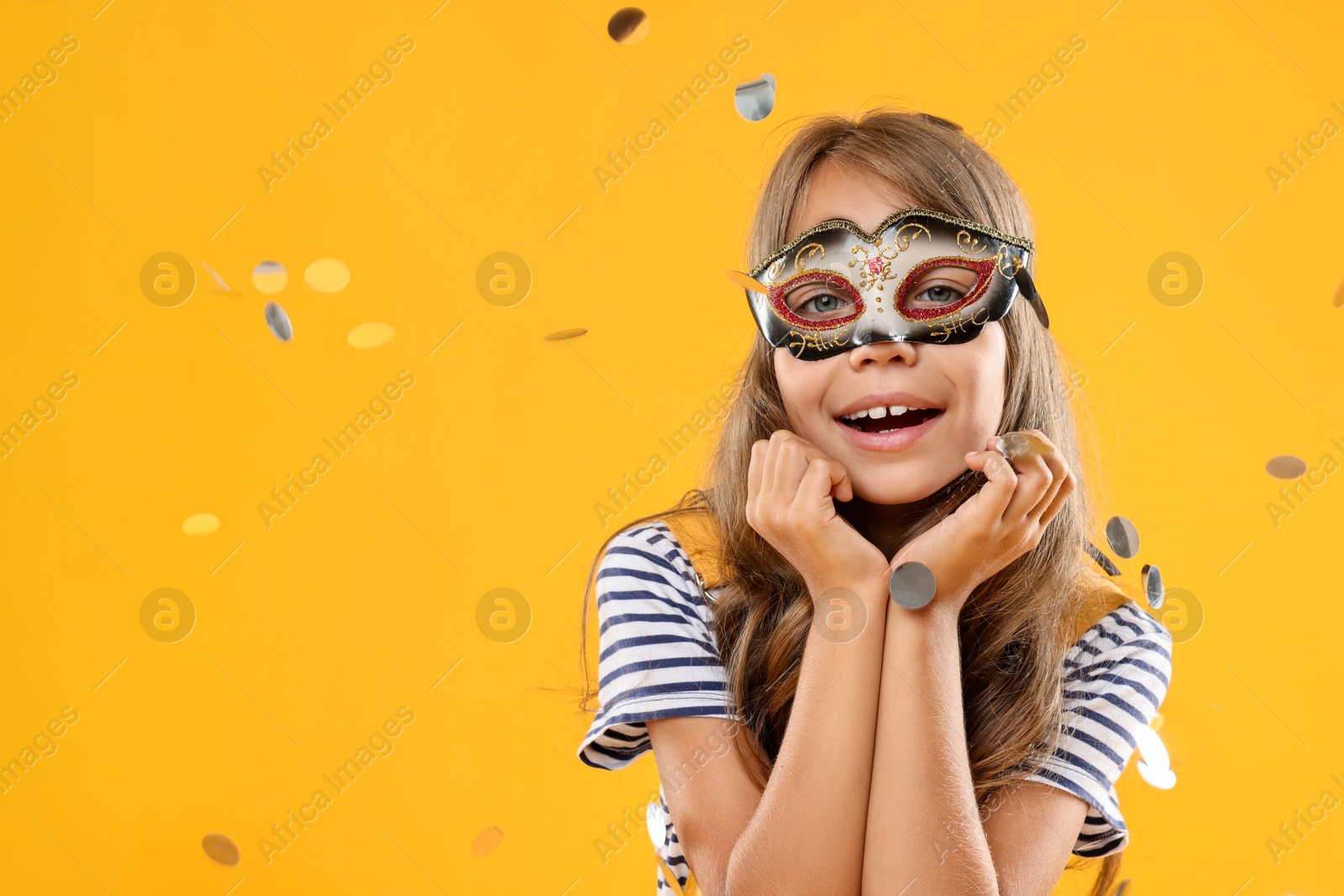 Photo of Cute girl wearing carnival mask and confetti on orange background, space for text