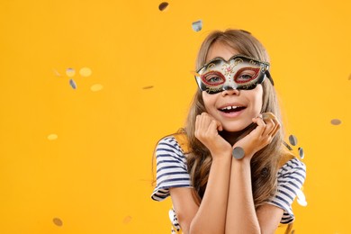 Cute girl wearing carnival mask and confetti on orange background, space for text