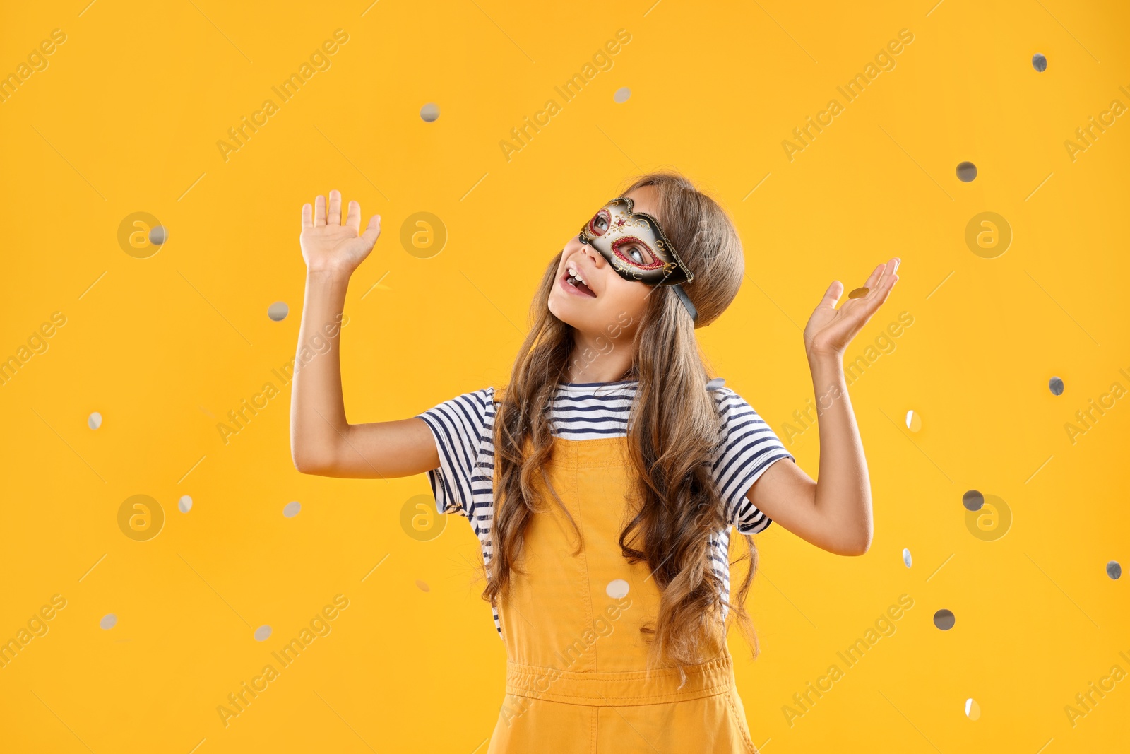 Photo of Cute girl wearing carnival mask and confetti on orange background