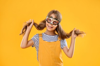 Photo of Cute girl wearing carnival mask on orange background