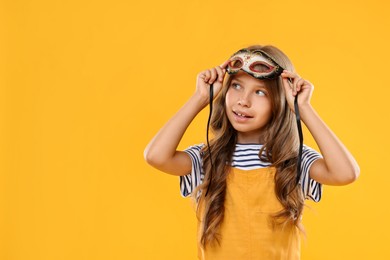 Photo of Cute girl wearing carnival mask on orange background, space for text