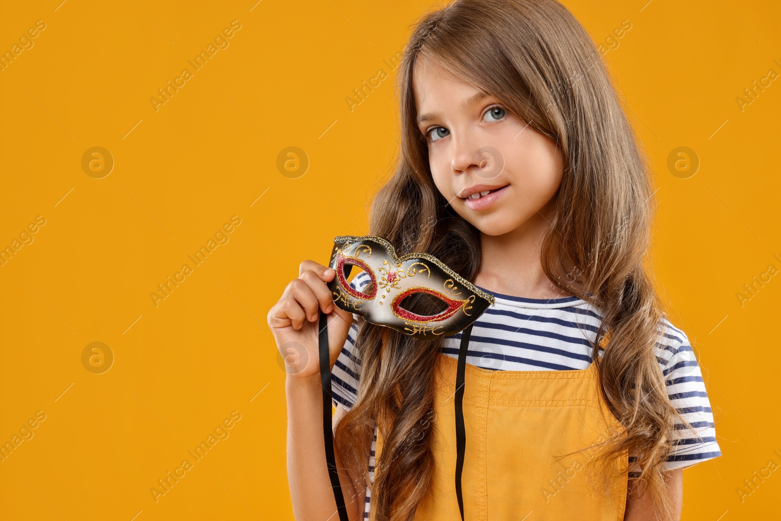 Photo of Cute girl with carnival mask on orange background, space for text