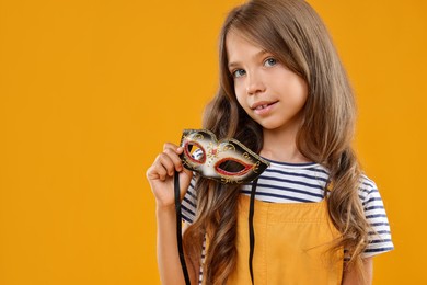 Photo of Cute girl with carnival mask on orange background, space for text