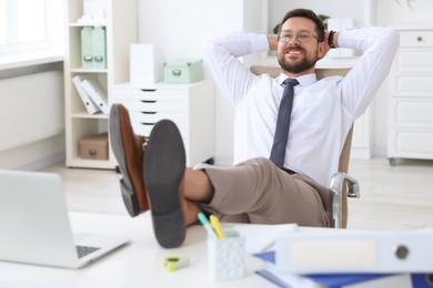 Smiling businessman with hands behind his head holding legs on table in office. Break time