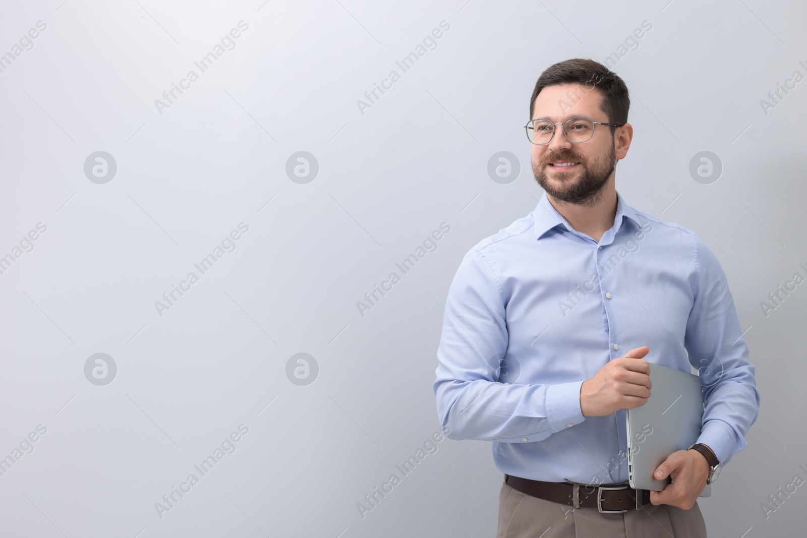 Photo of Portrait of smiling businessman with laptop on grey background. Space for text